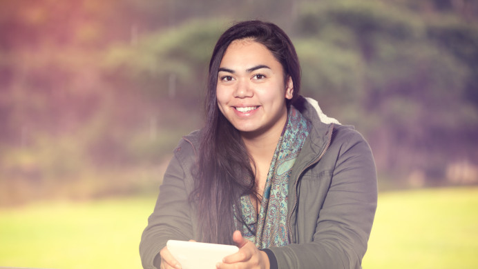 Young Māori woman smiling while looking at camera and using her smart device.