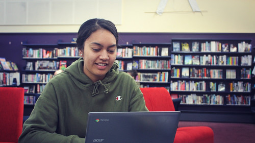 High school student looking at her laptop in a library