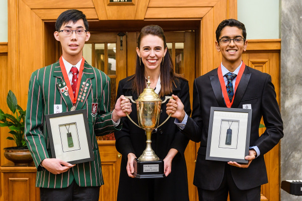 George Yang and Rohan Kumar smiling and holding the Prime Minister's Award for Academic Excellence trophy with the Prime Minister, Rt Hon Jacinda Ardern.