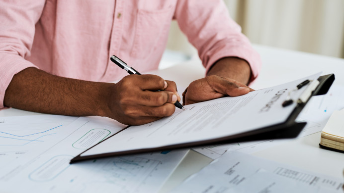 A man's hands are holding a clipboard and a pen