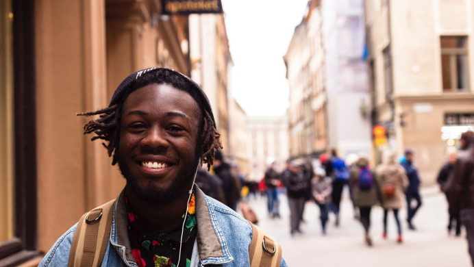 A young Black man stands smiling in the European city setting.