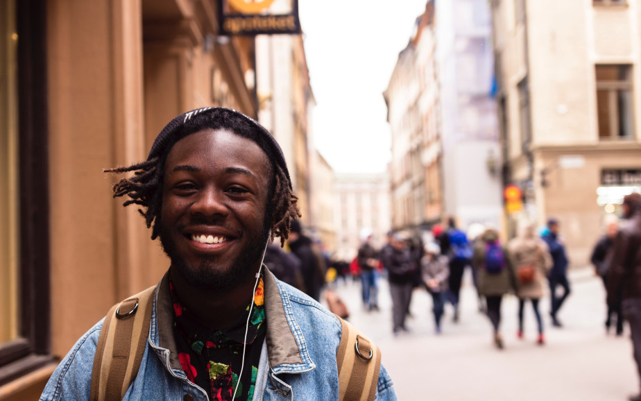 A young Black man stands smiling in the European city setting.