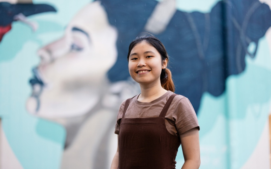 An international student stands in front of a mural