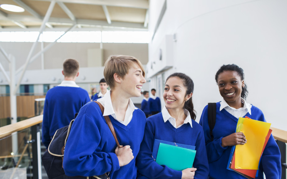 Three students in a blue uniform laugh together in a corridor