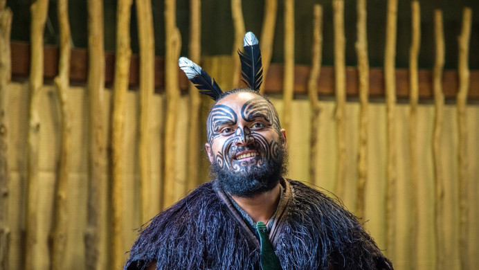 Māori tane wearing korowai, pounamu and feathers and ta moko smiles 