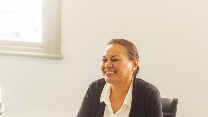 A wahine businesswoman smiles. She is sitting in an office.