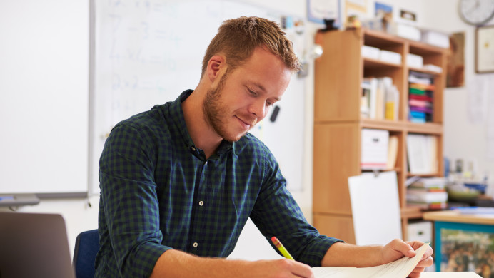A young male teacher works at his desk