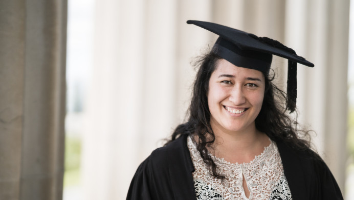 A smiling graduate is dressed in a gown