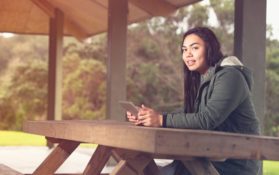 A young person sits at a park table with their phone.