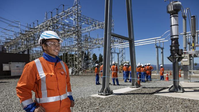 A woman stands at a power plant wearing high-vis.