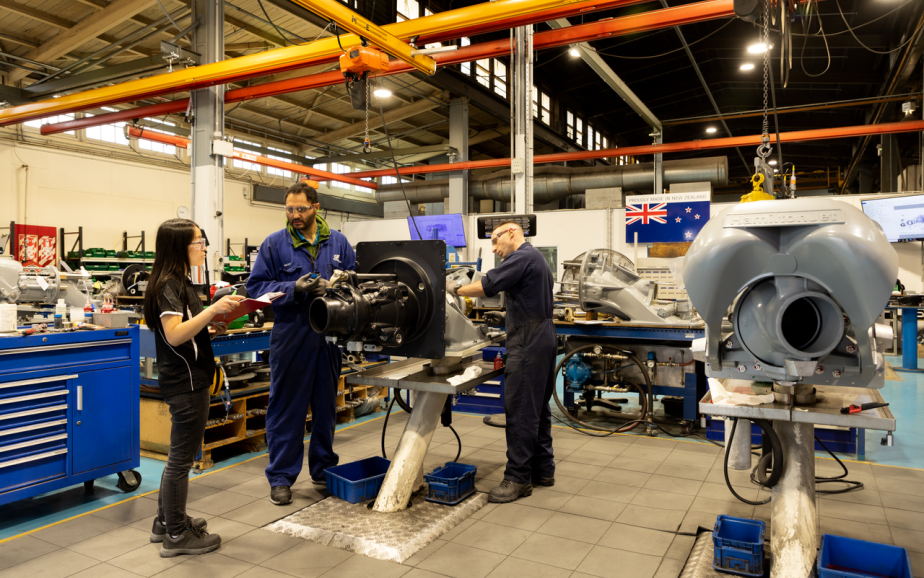 A tutor teaches students how to operate a machine in a workshop