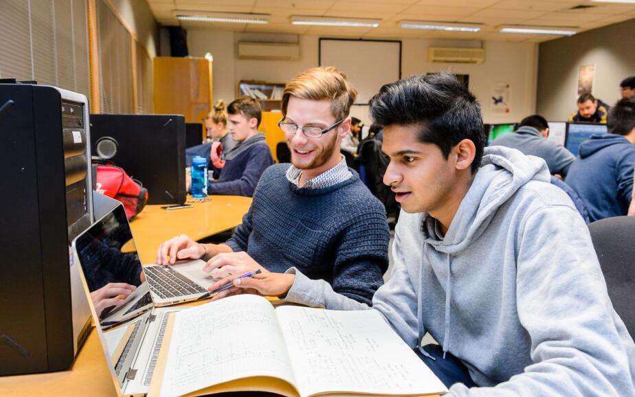 Two tertiary students at a PTE look at calculations on a computer